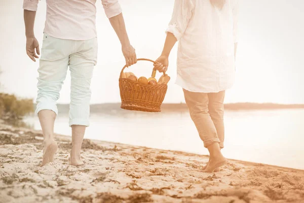 Adult couple walks along the seashore holding a basket of food — Stock Photo, Image