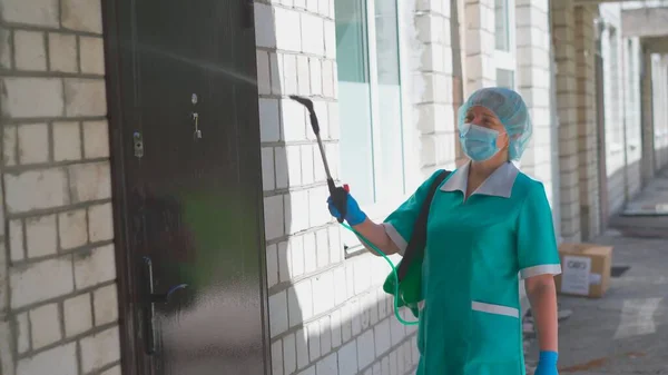 Lucrătorul mascat spală ușa și peretele de cărămidă al clădirii din spray antiseptic. Conceptul de tratament antiseptic. Tratament medical preventiv. Spitalul Municipal. Mai, 2020, Brovary, Ucraina — Fotografie, imagine de stoc