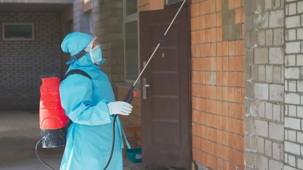 Koruyucu kıyafetli bir kadının binanın dış duvarını dezenfekte edişinin yan görüntüsü. Antiseptikle yapılan önleyici tıbbi tedavi. Şehir Hastanesi. Mayıs 2020, Brovary, Ukrayna — Stok fotoğraf