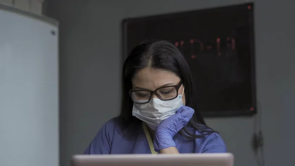 Medicul obosit lucrează cu un computer. Femeia cu masca de protectie si-a sustinut capul in mana uitandu-se la ecranul computerului. Conceptul de doctor epuizat — Fotografie, imagine de stoc