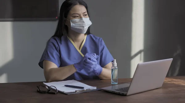 Médica trabalha com computador. Trabalhador médico de uniforme esfrega as mãos com um anti-séptico antes de trabalhar com laptop enquanto olha cansativamente pela janela — Fotografia de Stock
