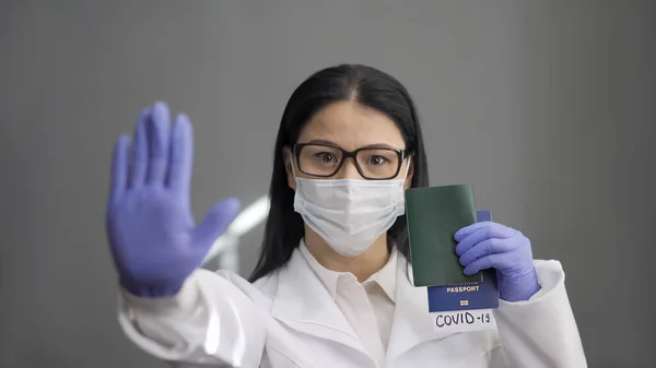 El doctor muestra una señal de stop con pasaportes. Mujer con uniforme protector sostiene pasaportes en su mano con inscripciones covid-19 en marcadores que extienden su otra palma abierta hacia adelante —  Fotos de Stock