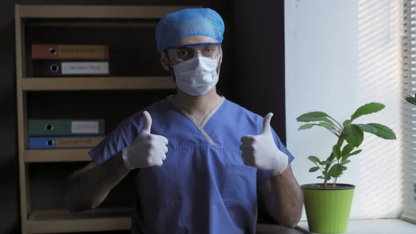 Doctorul îi arată lui Thumbs gestul. Gesturi pozitive de la un medic de sex masculin care stă lângă fereastră pe fundalul unui cabinet medical. Conceptul de finalizare pandemică — Fotografie, imagine de stoc