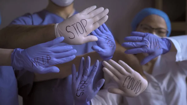 Baggrund fra hænderne på læger med åbne håndflader i flerfarvede engangshandsker med indskrifterne stopper covid test hjælp på dem. Pandemisk koncept - Stock-foto