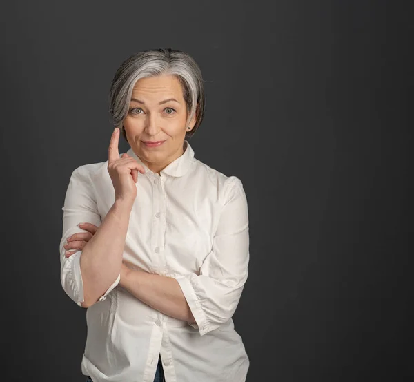 Have idea gesture from mature woman. Gray-haired businesswoman raised her index finger up while looking at camera posing on grey background Copyspace at right side. Eureka concept. Attention concept — Stock Photo, Image