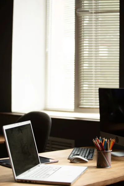 Escritorio de oficina con ordenador portátil, tableta digital y caja de lápices multicolores. Oficina de trabajo cerca de ventana —  Fotos de Stock