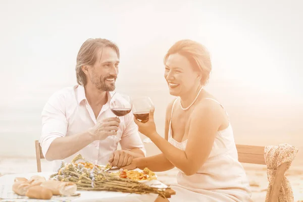 Feliz hombre y mujer beber vino tinto en la cafetería junto al mar al aire libre. Sonriente pareja de mediana edad tienen fecha sentado de la mano cerca del mar. Imagen tonificada —  Fotos de Stock