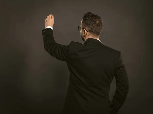 Un homme d'affaires intelligent écrit à la craie sur un mur noir. Vue arrière du cols blancs portant des lunettes en coffrage noir debout sur fond gris. Espace de copie pour le texte sur le côté gauche — Photo