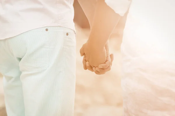 Pár se drží za ruce u moře. Zadní pohled muž a žena v jasných šatech drží ruce Procházka spolu po pláži za slunečného dne. Záběr zblízka. Izolovaný obrázek — Stock fotografie