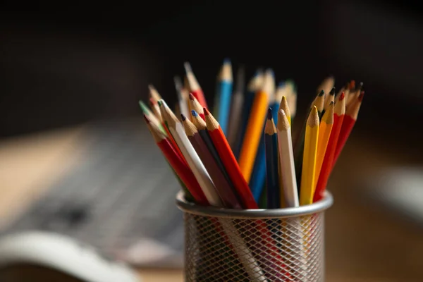 Office workplace. Focus on multi-colored pencils in foreground at wooden table with laptop computer on it. Copty space for text at left side. Close up shot — Stock Photo, Image