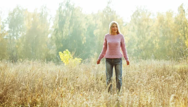 Okouzlující blondýnka stojící sama na trávníku mezi podzimní a letní přírodou podsvícenou sluncem. Koncept relaxace, Koncept svobody — Stock fotografie