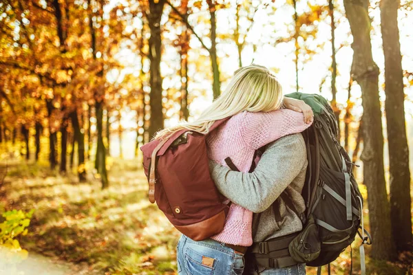 Abrazo de pareja de viajeros, hombre y mujer con mochilas abrazándose mientras están de pie en el bosque de otoño. Copiar espacio en el lado izquierdo — Foto de Stock