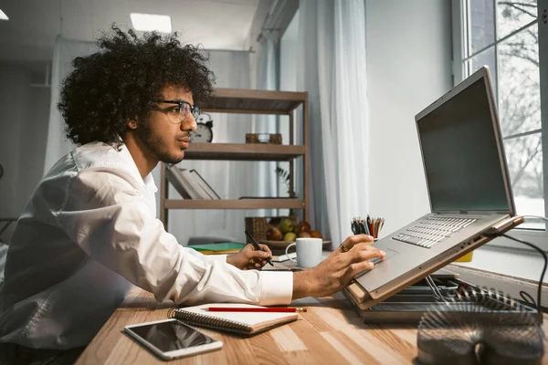 Lugar de trabajo del diseñador cerca de ventana. Inteligente creativo milenial trabajando con la computadora en un nuevo proyecto. Los hombres de negocios trabajan desde casa. Concepto de oficina en casa. Imagen tonificada — Foto de Stock