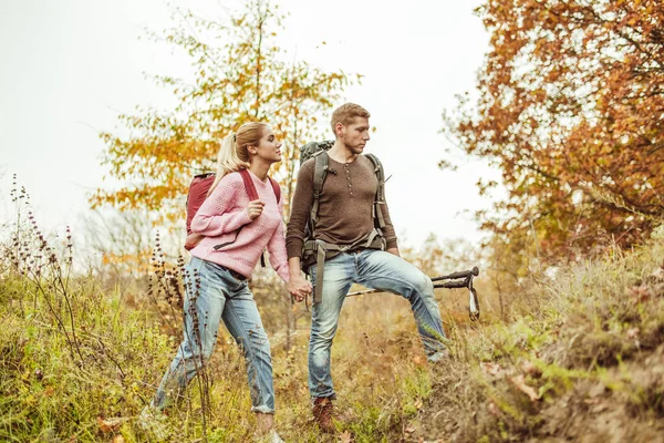 Turyści przedzierający się przez wzgórza trzymający się za ręce. Młoda para zakochanych ludzi sprawdza siłę ich związku podczas podróży w dziczy. Koncepcja turystyki pieszej — Zdjęcie stockowe