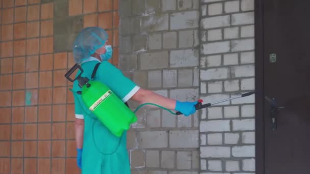 보호용 양복을 입은 여자의 측면 사진 이 건물의 외부 벽을 소독 한다. 살균제를 이용하여 건물을 짓는 예방 치료. 시립 병원. 2020 년 5 월, 우크라이나 브로바리 — 비디오