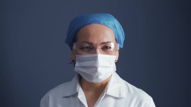 Zoom κάμερα πάνω από γιατρό γυναίκα σε προστατευτική μάσκα και γυαλιά φορώντας ιατρική στολή απομονώνονται σε σκούρο μπλε φόντο. Ιατρική έννοια. Πρότυπα 422 — Αρχείο Βίντεο