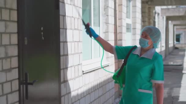 El trabajador sostiene un desinfectador de dispositivos mirando a la cámara, de pie contra la pared de ladrillo en la entrada del edificio en un día soleado. Concepto de limpieza. Hospital municipal. mayo, 2020, Brovary, Ucrania — Vídeos de Stock