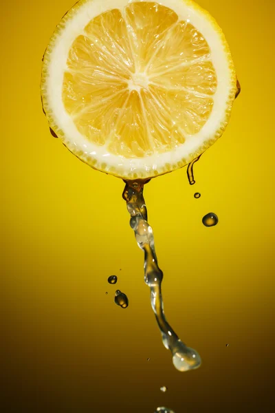 Fatia de limão e salpico de suco isolado no fundo laranja — Fotografia de Stock