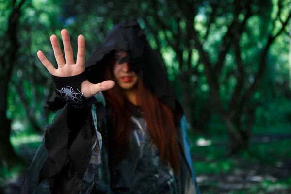 Picture of witch in black cloak with outstretched hand in forest