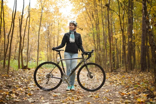 Image of girl in helmet, jeans next to bicycle in autumn park — Stock Photo, Image