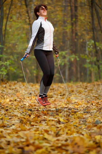 Side view of sporty woman jumping with rope at autumn forest — Stock Photo, Image