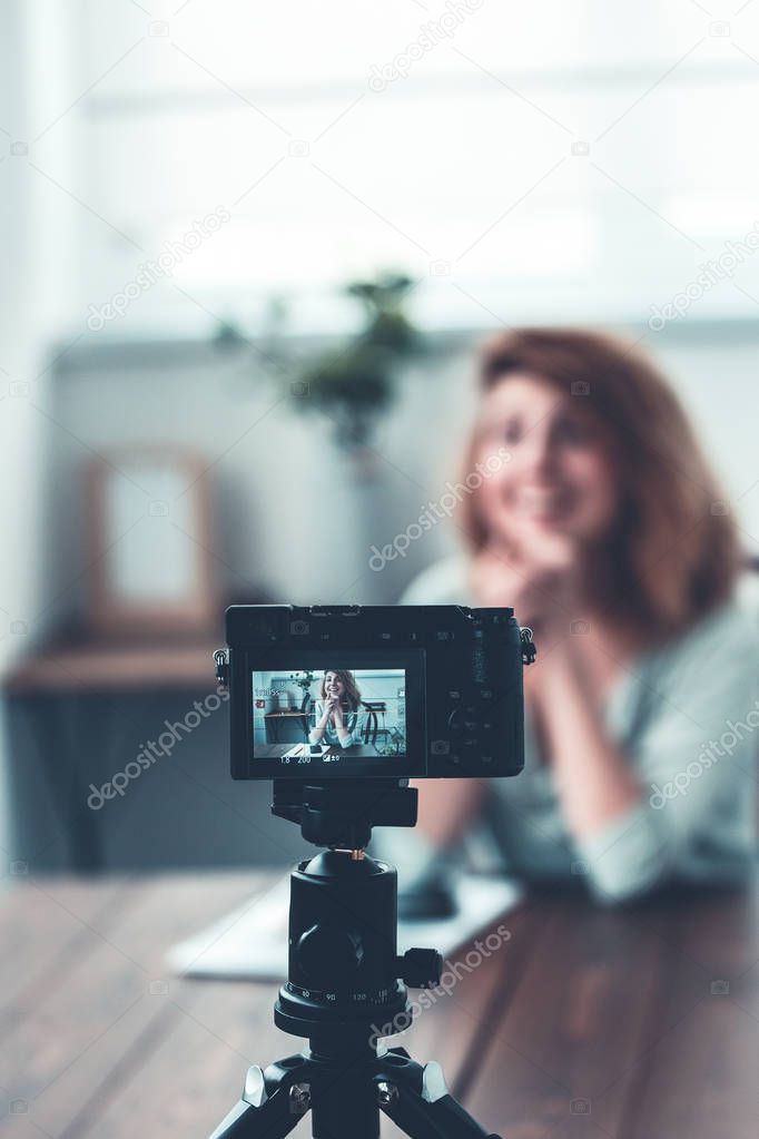 Bokeh photo of cheerful female florist sitting on table with succulent in glass jar.