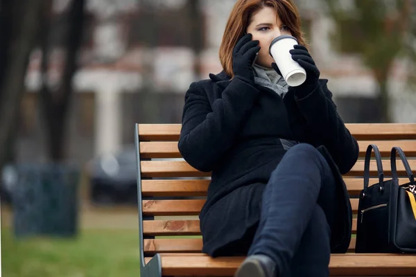 Фото девушки в черном пальто, разговаривающей по телефону и пьющей кофе — стоковое фото