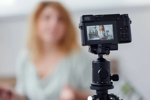 Imagem turva de mulher blogueira à mesa com florário. Tiro master class na câmera de vídeo — Fotografia de Stock