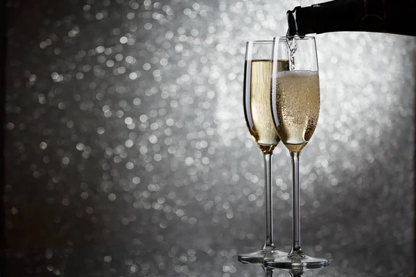 Photo of bottle with pouring champagne in wine glasses on gray background — Stock Photo, Image