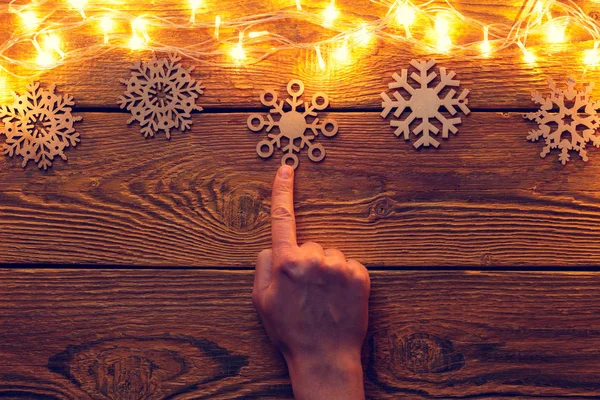 Photo of wooden surface with burning garland from above, snowflakes, hand pointing upwards. — Stock Photo, Image
