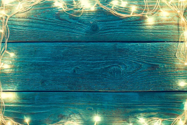 Foto der blauen Holzoberfläche mit brennenden Neujahrsgirlanden um den Umkreis. — Stockfoto