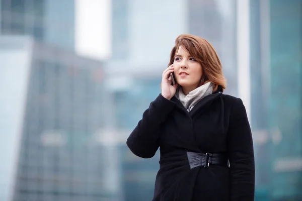 Image of brunette in black coat talking on phone in modern building — Stock Photo, Image