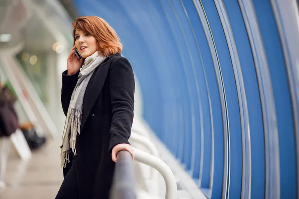 Beeld van de vrouw in zwarte jas praten over telefoon in modern gebouw — Stockfoto