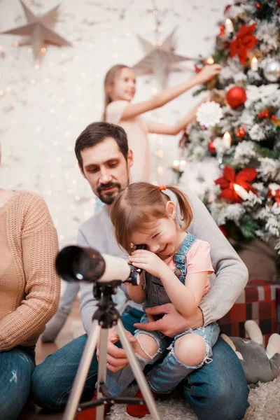 Beeld van ouders en dochters met telescoop op achtergrond van ingerichte New Years-zilverspar — Stockfoto