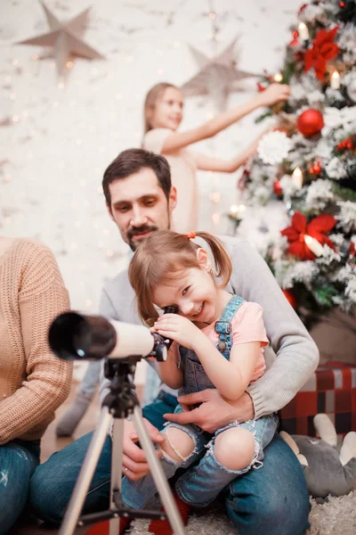 Foto van ouders en dochters met telescoop op achtergrond van ingerichte New Years-zilverspar — Stockfoto