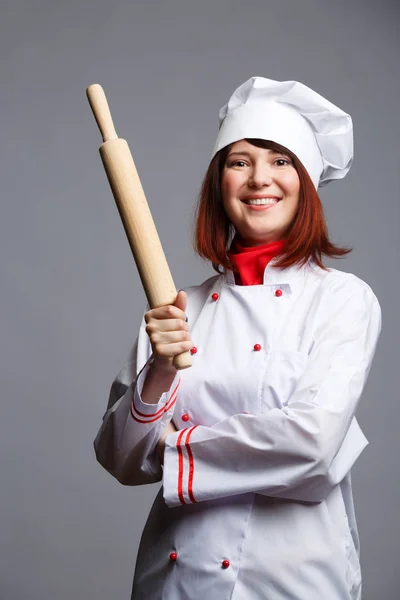 Foto van brunette chef-kok in witte robe en cap met deegroller in handen — Stockfoto