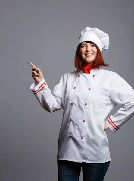 Imagem de chef morena sorridente em roupão branco apontando o dedo para o espaço vazio — Fotografia de Stock