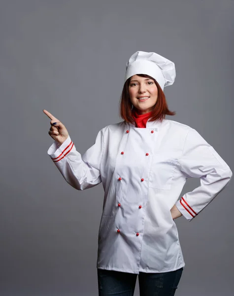 Foto de chef morena sorridente em roupão branco apontando o dedo para o espaço vazio — Fotografia de Stock