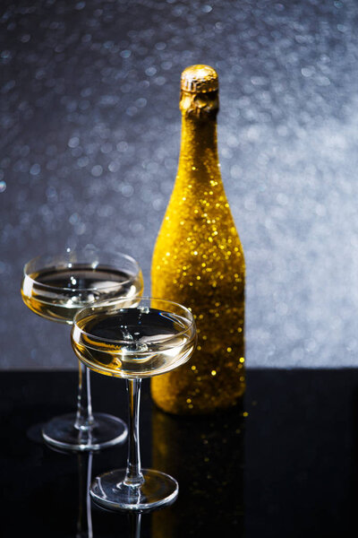 Праздничное изображение бутылки шампанского в золотой обертке с двумя бокалами вина
