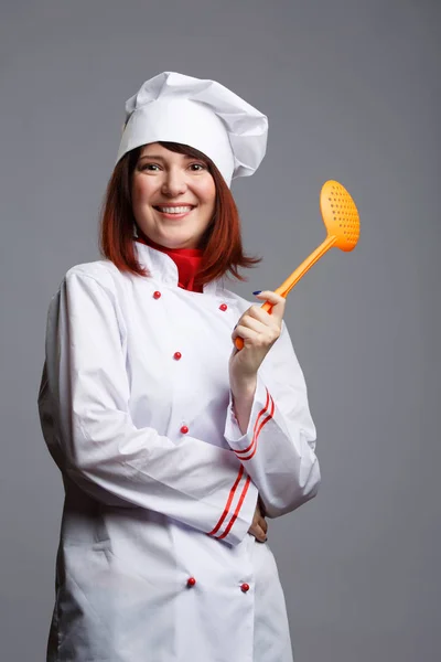 Mujer imagen cocina en bata blanca y gorra con cuchara ranurada en la mano — Foto de Stock