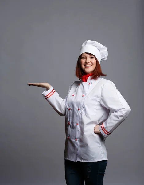 Imagem de chef morena sorridente em roupão branco com palma vazia — Fotografia de Stock