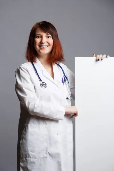 Női orvos fehér kabátot és phonendoscope képet mutat üres papírlapot ujját — Stock Fotó