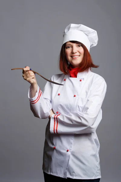 Photo of brunette chef in white robe and cap with wooden spoon