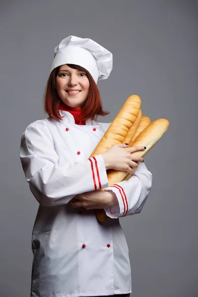 Φωτογραφία: μελαχρινή σεφ σε λευκό παλτό και καπάκι με Γαλλική μπαγκέτα στα χέρια — Φωτογραφία Αρχείου