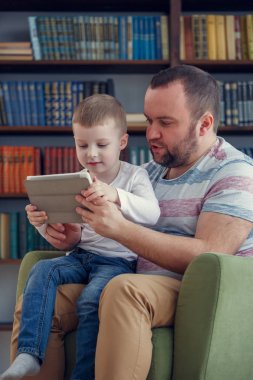 Baba ve küçük oğlu ile tablet yeşil sandalye üzerinde oturan resmi