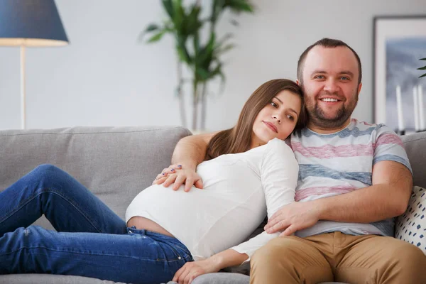 坐在灰色沙发上的幸福未来父母的照片 — 图库照片