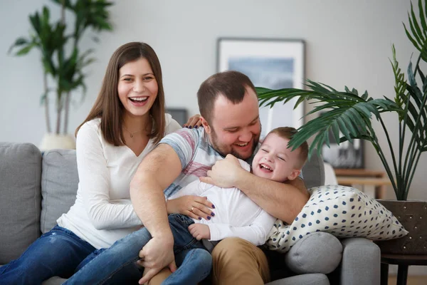 Family picture of happy parents and son sitting on gray sofa — Stock Photo, Image