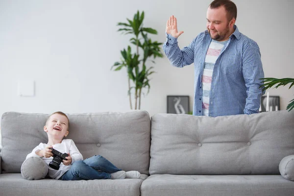 Сімейна фотографія молодого сина, що сидить з камерою в руках на сірому дивані і тато — стокове фото