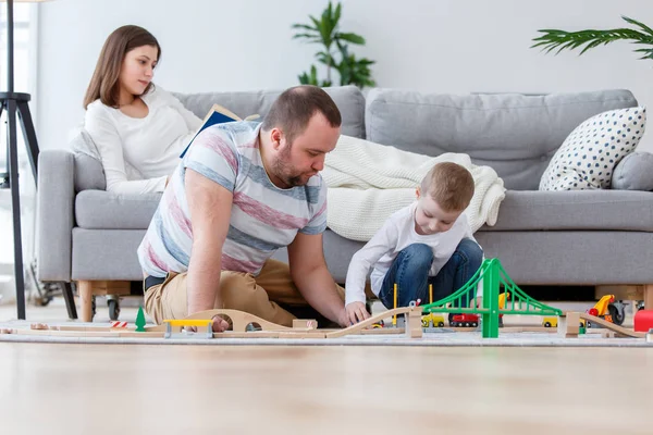 Imagen de padres felices con su hijo jugando a la carretera de juguete sentado en el suelo — Foto de Stock