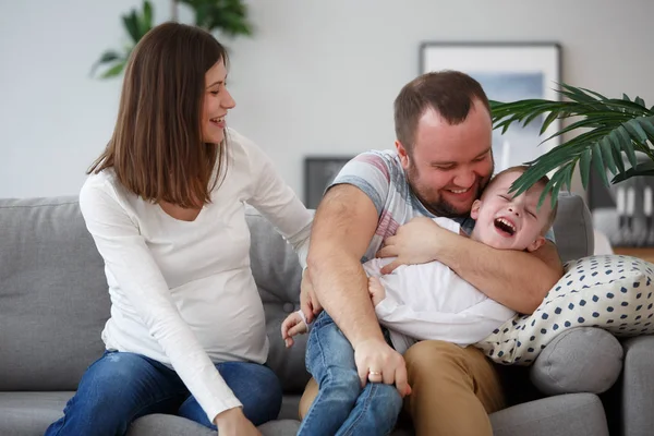 Picture of smiling parents with son sitting on gray sofa — Stock Photo, Image